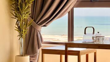 Een kamer met uitzicht op het strand, een tafel met theepot en kopjes, een bamboeplant en een geweven mat.