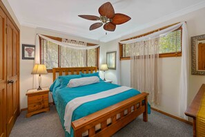 A bedroom with a wooden bed, a ceiling fan, two bedside tables with lamps, and a window with curtains. - Sandalwood - Two-bedroom holiday house surrounded by peaceful bushland (Dunbogan)