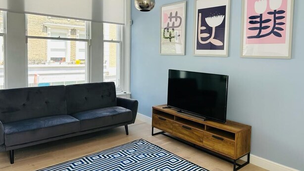 A living room with a black sofa, a TV on a wooden stand, and three framed artworks on the wall.