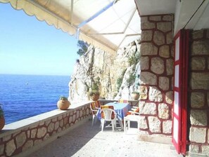 Enjoy the ocean view from this seaside terrace with a table and chairs, surrounded by potted plants.