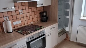 A modern kitchen with white cabinets, a built-in oven, a coffee maker, and a refrigerator. - Ferienwohnung Simon Platz für bis zu 4 Personen. Haustierfreundlich! (Diemelstadt)