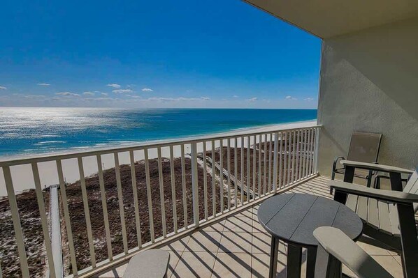 A balcony with a view of the ocean, a table, and two chairs.