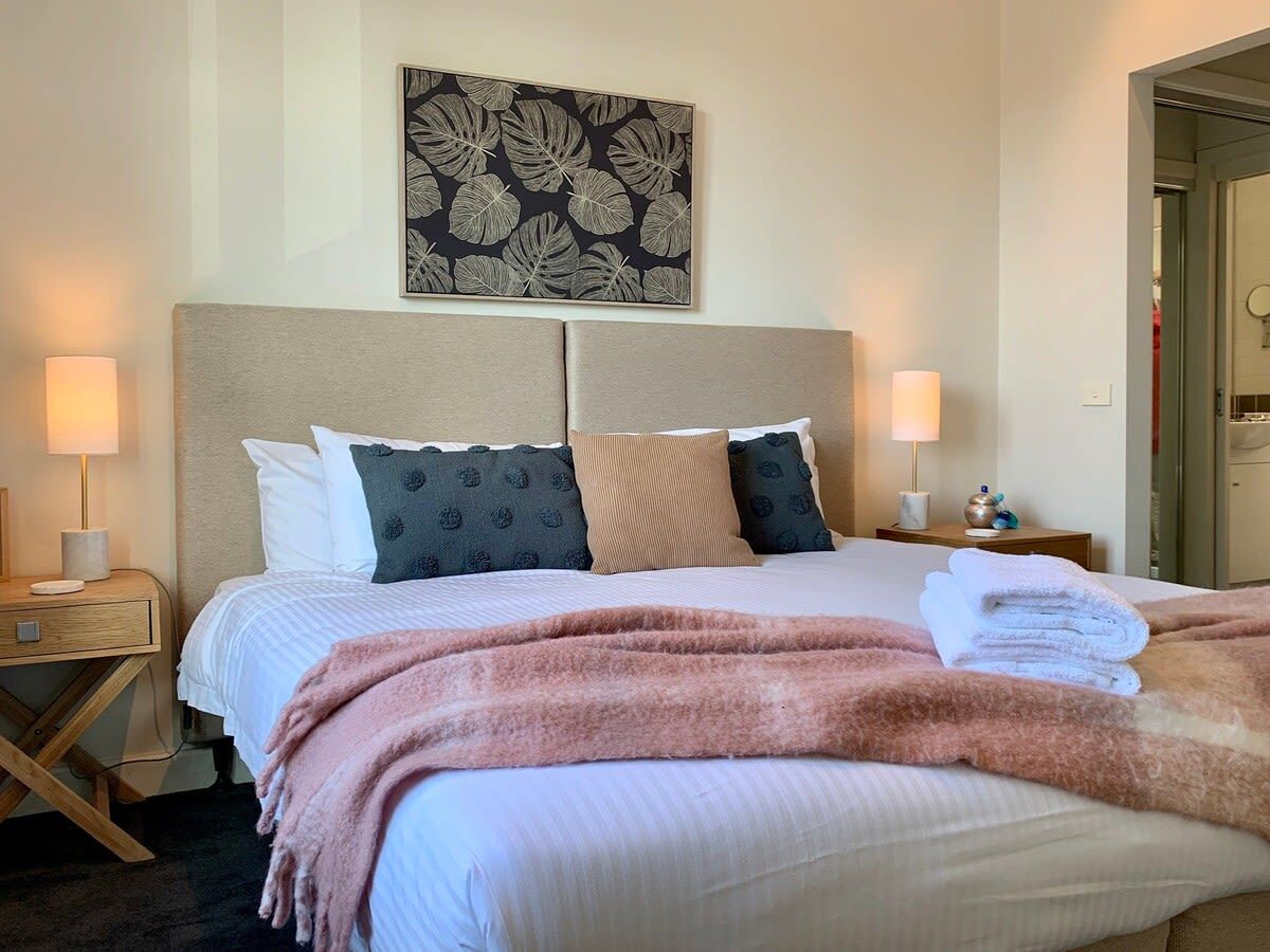 A neatly made bed with a headboard, two bedside tables with lamps, and a wall-mounted artwork.