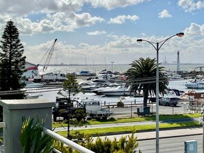 A marina with boats docked, a crane, and a distant view of a city skyline.