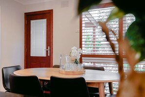Ruokailutila, jossa on pyöreä pöytä, tuoleja, puuovi ja ikkuna, jossa on sälekaihtimet.