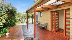 Un patio techado al aire libre con piso de madera, pared de ladrillo y puerta corrediza de vidrio que da a una habitación.