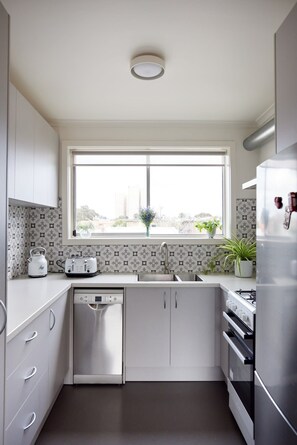 Cocina funcional con lavavajillas, horno empotrado, refrigerador y ventana con vistas al exterior.