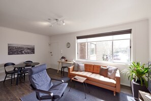 A modern living room with a sofa, chairs, a small table, and a large window with a view of the city.