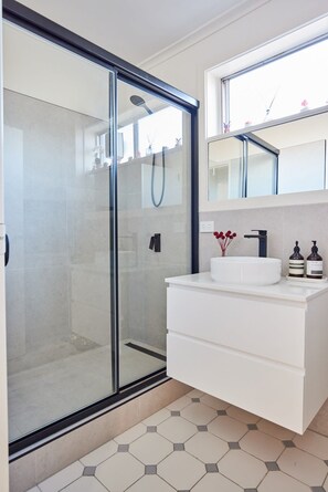 A modern bathroom with a glass shower enclosure, a white sink, and a mirror above the vanity.