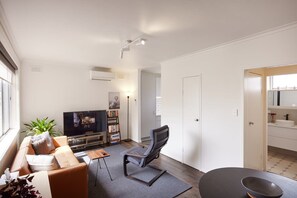 Una sala de estar moderna con un sofá, televisión, estantería y comedor con mesa y sillas.
