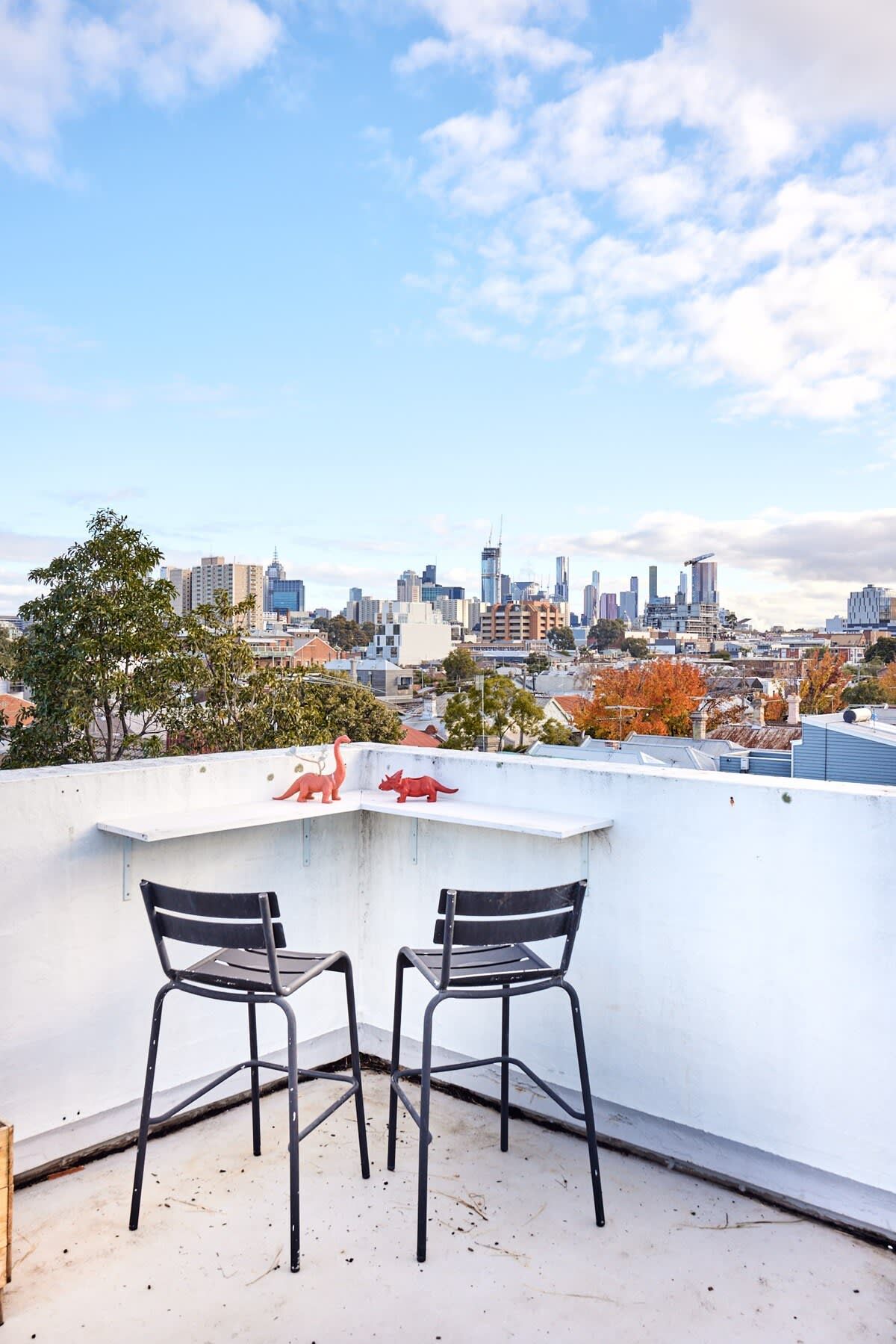 A rooftop terrace with two chairs, a small table, and a cityscape view.