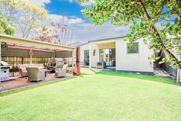 A backyard with a lawn, outdoor furniture, and a pergola.