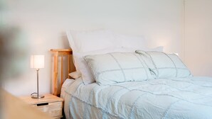 A neatly made bed with a light-colored duvet and pillows, a bedside table with a lamp, and a wooden headboard.