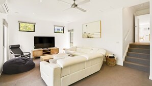 A modern living room with a sectional sofa, a flat-screen TV, a black bean bag, and a ceiling fan.