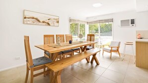 A dining area with a wooden table and chairs, a bench, and a view of greenery outside.
