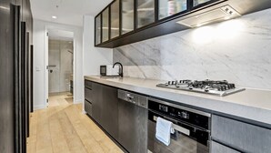 A modern kitchen with a marble countertop, stainless steel appliances, and a glass-fronted cabinet.