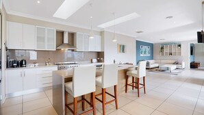 A modern kitchen with white cabinets, a central island with bar stools, and a dining area with a sofa and coffee table.