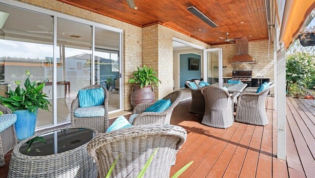 An outdoor patio with wicker furniture, a ceiling fan, and a brick wall.