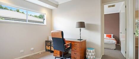Een slaapkamer met een bureau, stoel, lamp en een bed met uitzicht op groen.