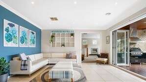 A modern living room with a sectional sofa, a coffee table, and a rug. There is a kitchen visible through a glass door.