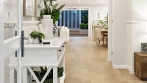 Un pasillo moderno y bien iluminado con armarios blancos y piso de madera, que conduce a un comedor con vistas a zonas verdes.