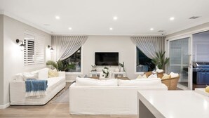 Una sala de estar moderna con un conjunto de sofá blanco, un televisor de pantalla plana y una zona de barbacoa.