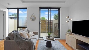 Un salon moderne avec un canapé gris, une table basse ronde et un téléviseur posé sur un meuble en bois.