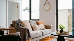 Un salon moderne avec un canapé, une petite table ronde agrémentée d’une plante et une grande fenêtre offrant une vue sur l’extérieur.