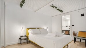 A modern bedroom with a bed, bedside lamps, a bench, and a mirror.