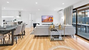 Ein modernes Wohnzimmer mit Essbereich, einer Couch, einem Couchtisch und einem an der Wand befestigten Fernseher.