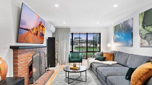 Ein modernes Wohnzimmer mit Kamin, einer Couch, einem Couchtisch und einem großen Fenster mit Blick ins Freie.