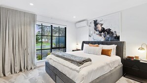 Ein modernes Schlafzimmer mit einem großen Bett, Blick ins Freie und einem abstrakten Kunstwerk an der Wand.