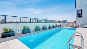Une piscine sur le toit, avec un ciel dégagé, un panneau indiquant une profondeur de 1,4 mètre et des chaises longues.