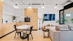 Une cuisine moderne avec des meubles blancs, un mur d ’accent en bois et un coin repas comprenant une table ronde et des chaises.