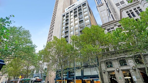 A street view with tall buildings, a tram, and trees.