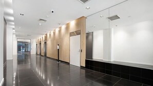 A modern, clean hallway with a polished black floor, wooden panel accents, and a glass door leading to an elevator.