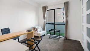 A modern room with a wooden desk, a sofa, a small table, and a window with curtains.