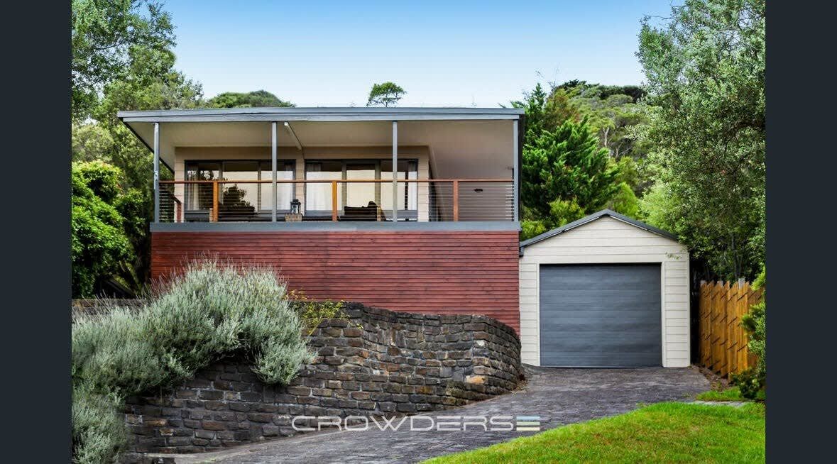 A modern two-story house with a balcony, a garage, and a stone wall.