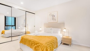 A modern bedroom with a large bed, a bedside table, a mirror, and a framed artwork on the wall.
