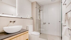 A modern bathroom with a large white sink, a toilet, and a glass-enclosed shower area.