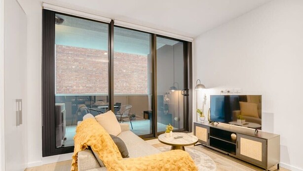 A modern living room with a sofa, a TV, and a sliding glass door leading to an outdoor area.