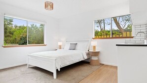 Un dormitorio con cama, mesitas de noche, ventana y vista a zonas verdes.