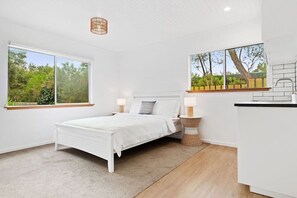 A bedroom with a bed, bedside tables, a window, and a view of greenery.