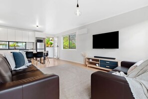 A modern living room with a sofa, a TV, and a dining area with chairs and a table.