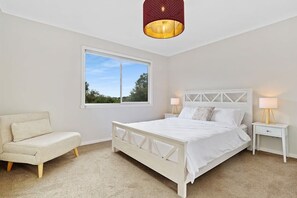 A bedroom with a bed, a nightstand, a lamp, a chair, and a window.