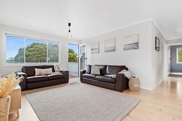 A spacious living room with two dark brown leather sofas, a large grey rug, and a wooden coffee table.