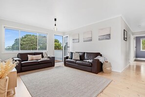 Ein geräumiges Wohnzimmer mit zwei dunkelbraunen Ledersofas, einem großen grauen Teppich und einem Holztisch.