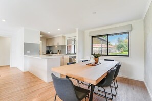 A modern kitchen with white cabinets, a wooden dining table, and a large window with a view of a residential area.