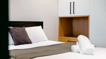 A hotel room with a bed, a wooden wardrobe, and a rolled-up towel on the bed.