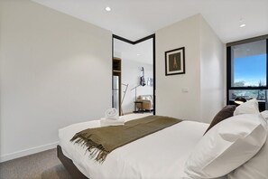 Een moderne hotelkamer met een groot bed, een uitzicht door een raam en een spiegel die de kamer weerspiegelt.